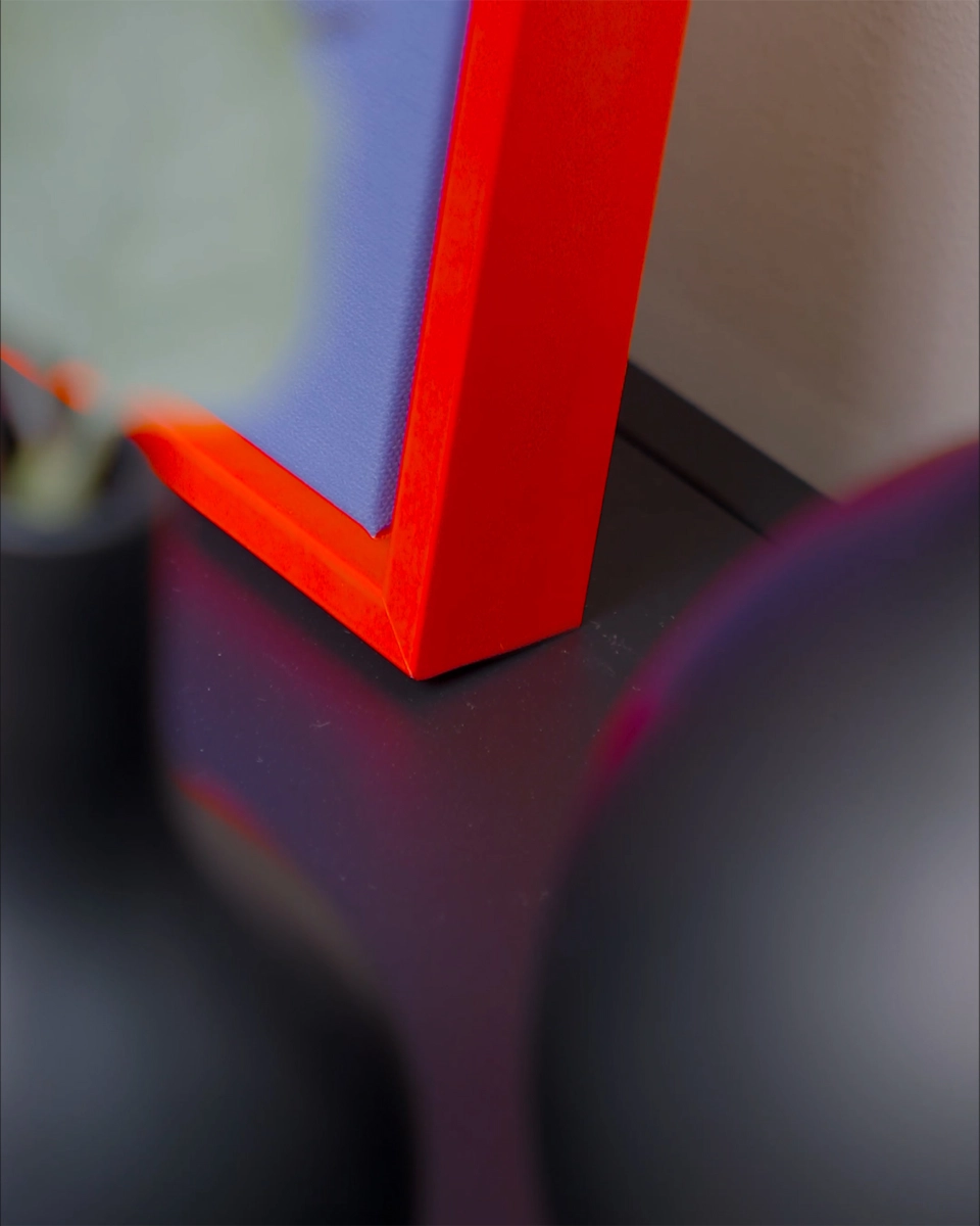 Gros plan sur l’angle du cadre de type caisse américaine Jill en rouge néon éclatant pour toiles, dans un intérieur chaleureux.
